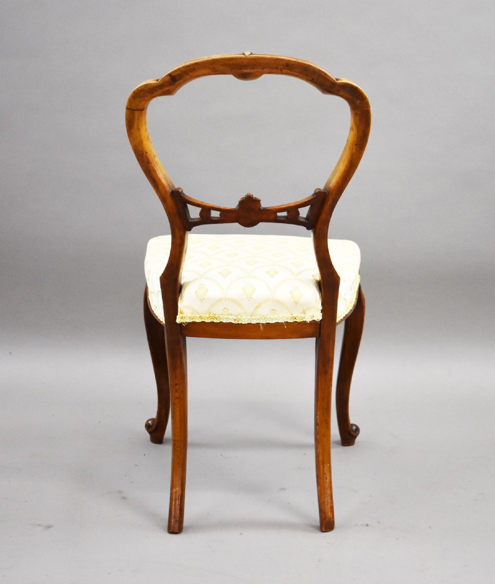 A set of four Victorian walnut balloon back dining chairs with carved horizontal splats, cabriole front legs, and cream pattern upholstered seats. View VII