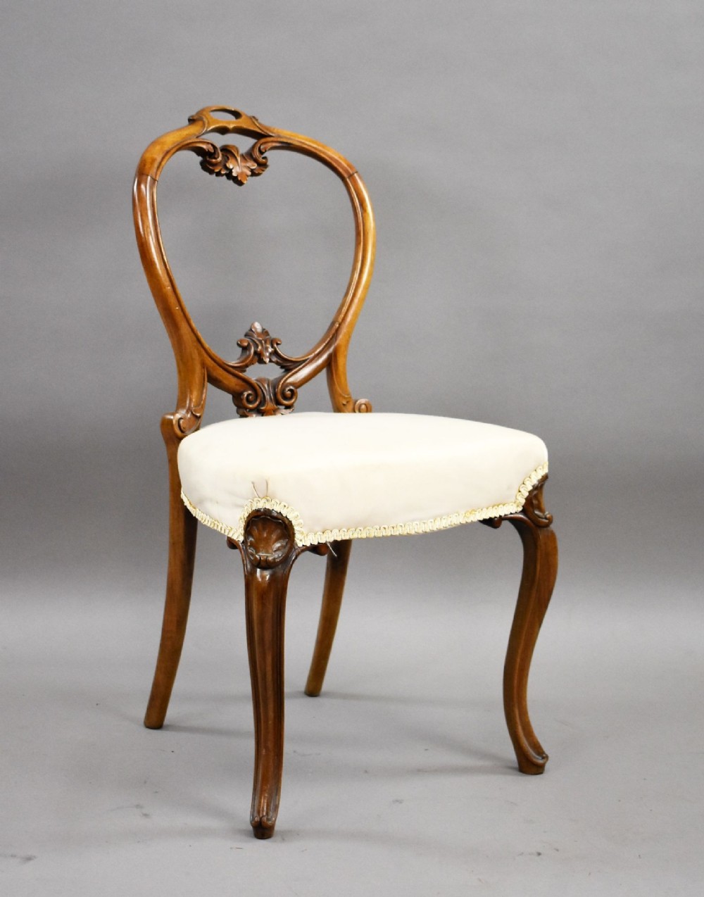 A set of four Victorian walnut balloon back dining chairs featuring carved back crests, cabriole front legs, and cream upholstered seats. View II