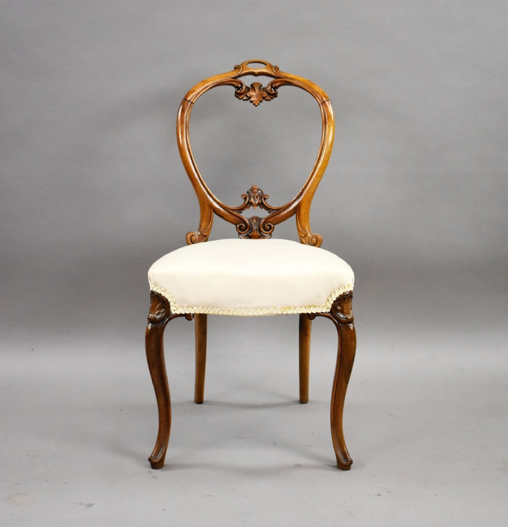 A set of four Victorian walnut balloon back dining chairs featuring carved back crests, cabriole front legs, and cream upholstered seats. View III