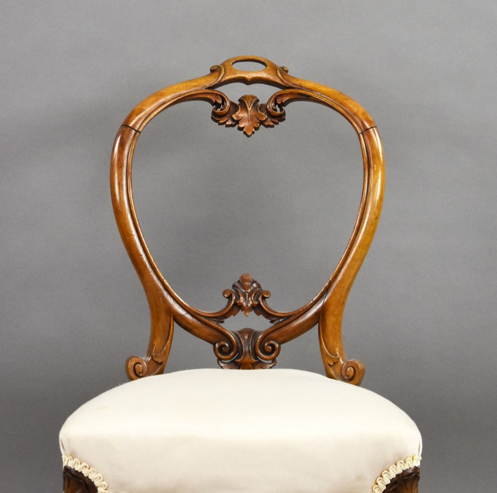 A set of four Victorian walnut balloon back dining chairs featuring carved back crests, cabriole front legs, and cream upholstered seats. View IV