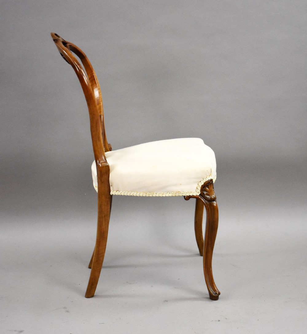 A set of four Victorian walnut balloon back dining chairs featuring carved back crests, cabriole front legs, and cream upholstered seats. View VI