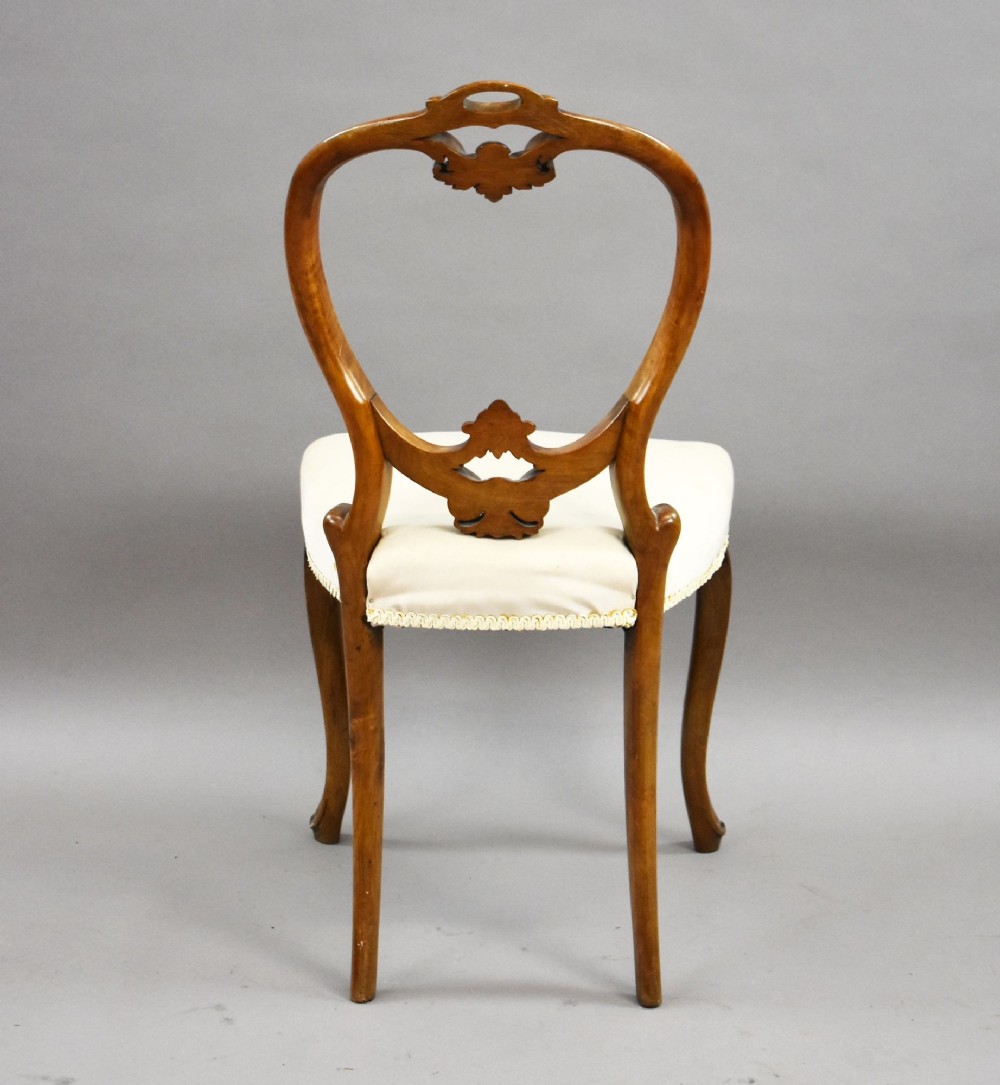 A set of four Victorian walnut balloon back dining chairs featuring carved back crests, cabriole front legs, and cream upholstered seats. View VII