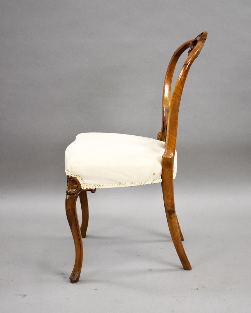 A set of four Victorian walnut balloon back dining chairs featuring carved back crests, cabriole front legs, and cream upholstered seats. View VIII