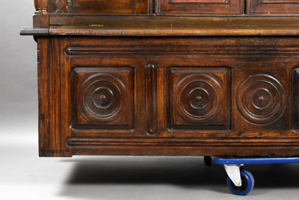 A high-backed dark oak panelled settle featuring geometric roundel carvings, a spindle frieze, scroll arms, and a box seat storage base. View VII