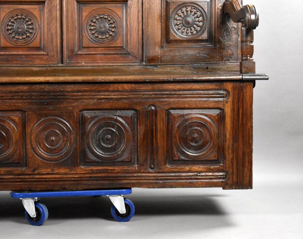 A high-backed dark oak panelled settle featuring geometric roundel carvings, a spindle frieze, scroll arms, and a box seat storage base. View VIII