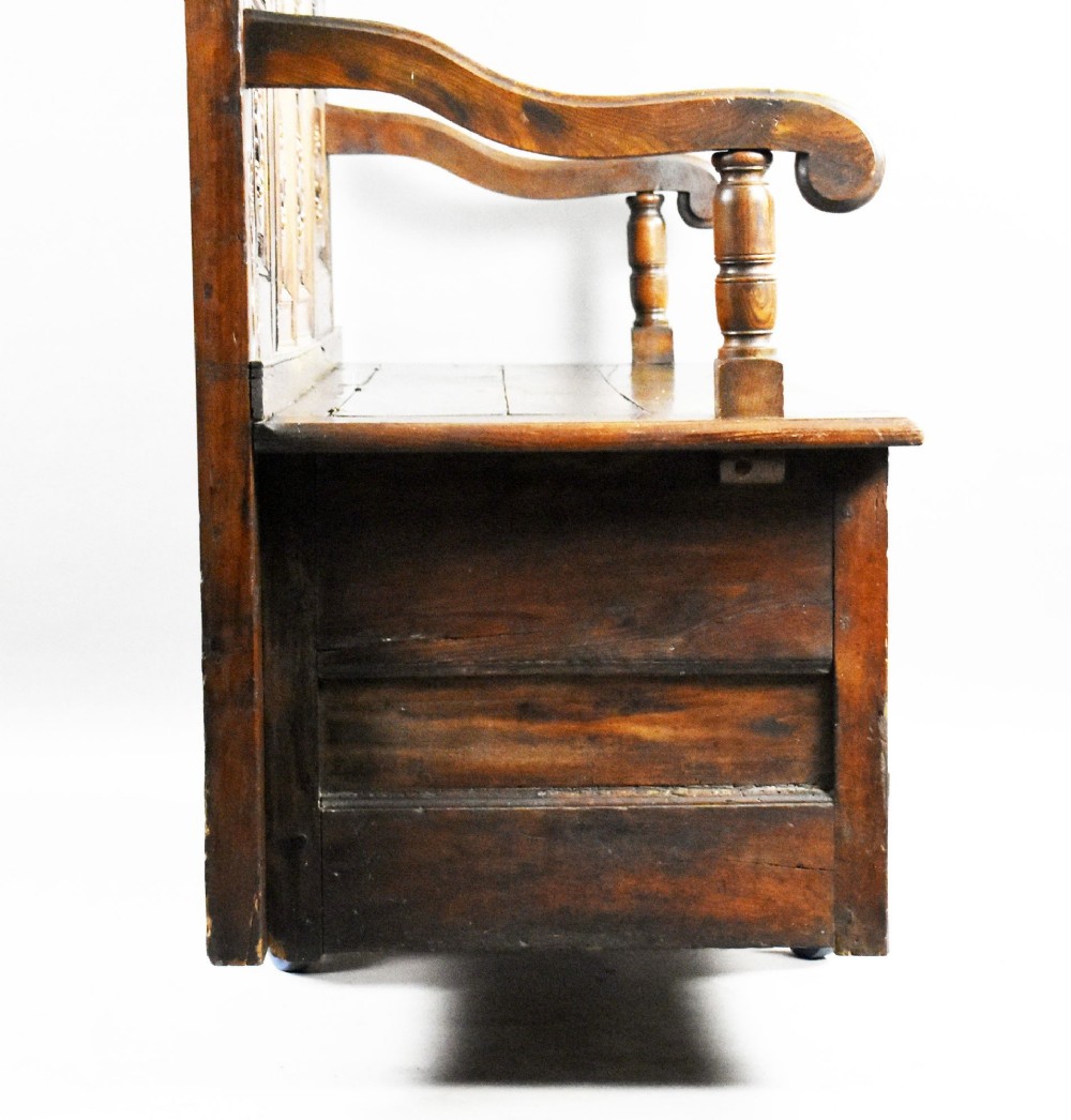 A high-backed dark oak panelled settle featuring geometric roundel carvings, a spindle frieze, scroll arms, and a box seat storage base. View XI