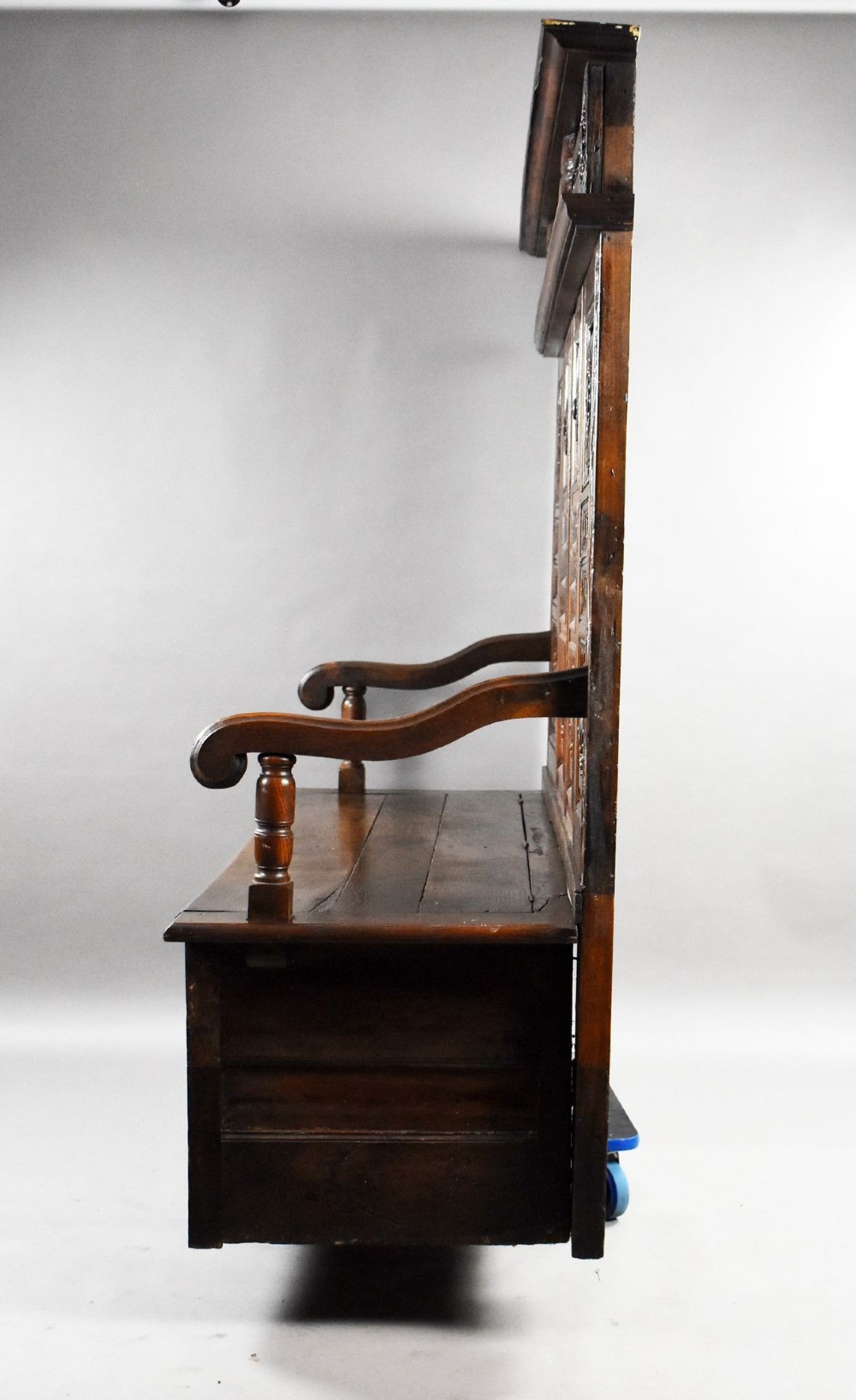A high-backed dark oak panelled settle featuring geometric roundel carvings, a spindle frieze, scroll arms, and a box seat storage base. View XII