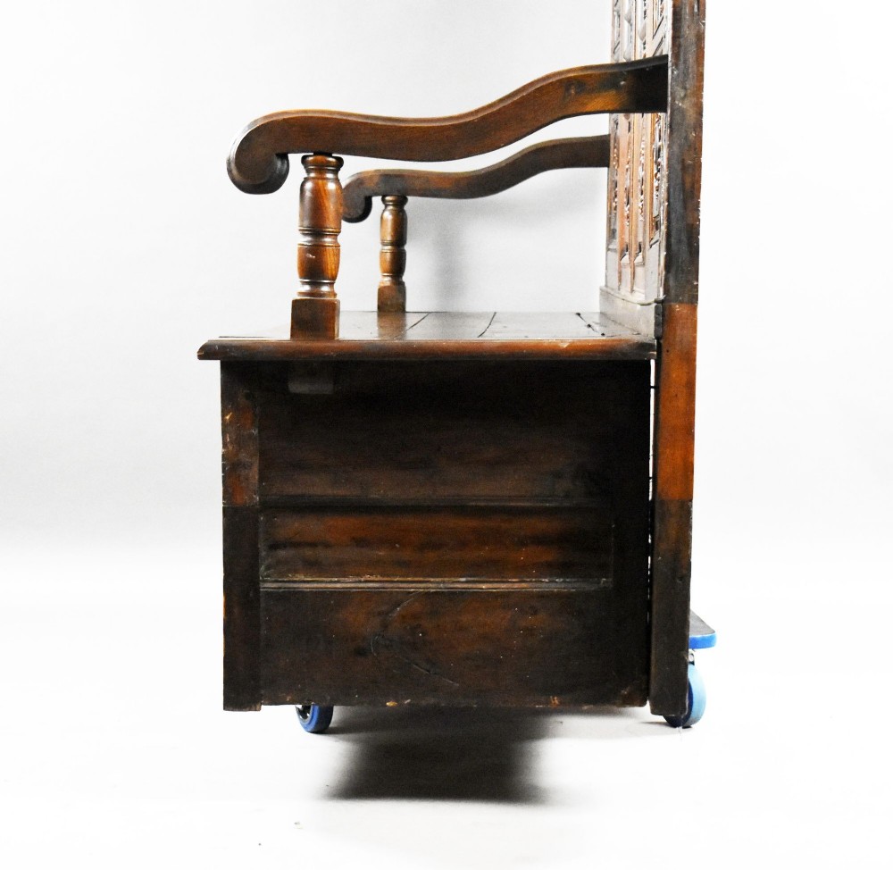 A high-backed dark oak panelled settle featuring geometric roundel carvings, a spindle frieze, scroll arms, and a box seat storage base. View XIII