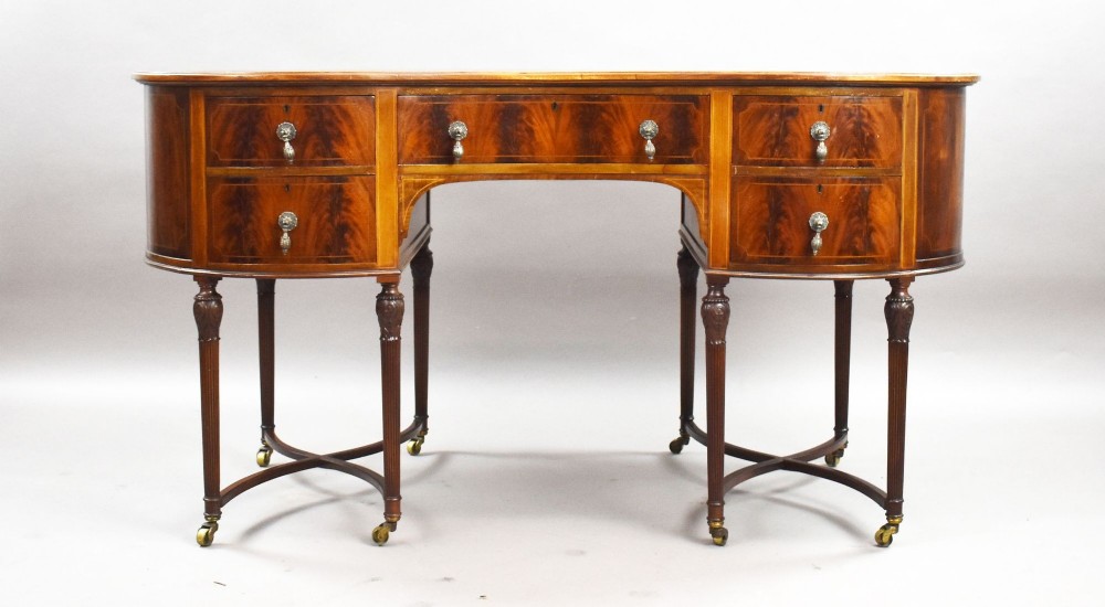 An Edwardian kidney-shaped writing desk crafted from flame mahogany with a green leather writing surface, five drawers, turned fluted legs, and brass castors. View III