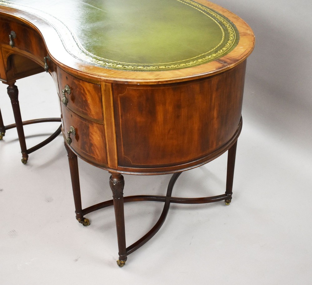An Edwardian kidney-shaped writing desk crafted from flame mahogany with a green leather writing surface, five drawers, turned fluted legs, and brass castors. View VII
