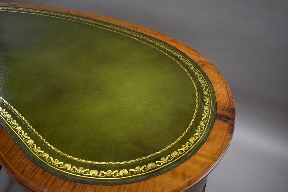 An Edwardian kidney-shaped writing desk crafted from flame mahogany with a green leather writing surface, five drawers, turned fluted legs, and brass castors. View VIII