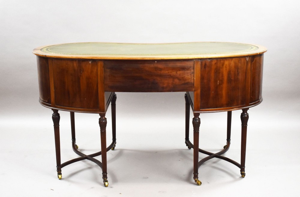 An Edwardian kidney-shaped writing desk crafted from flame mahogany with a green leather writing surface, five drawers, turned fluted legs, and brass castors. View IX