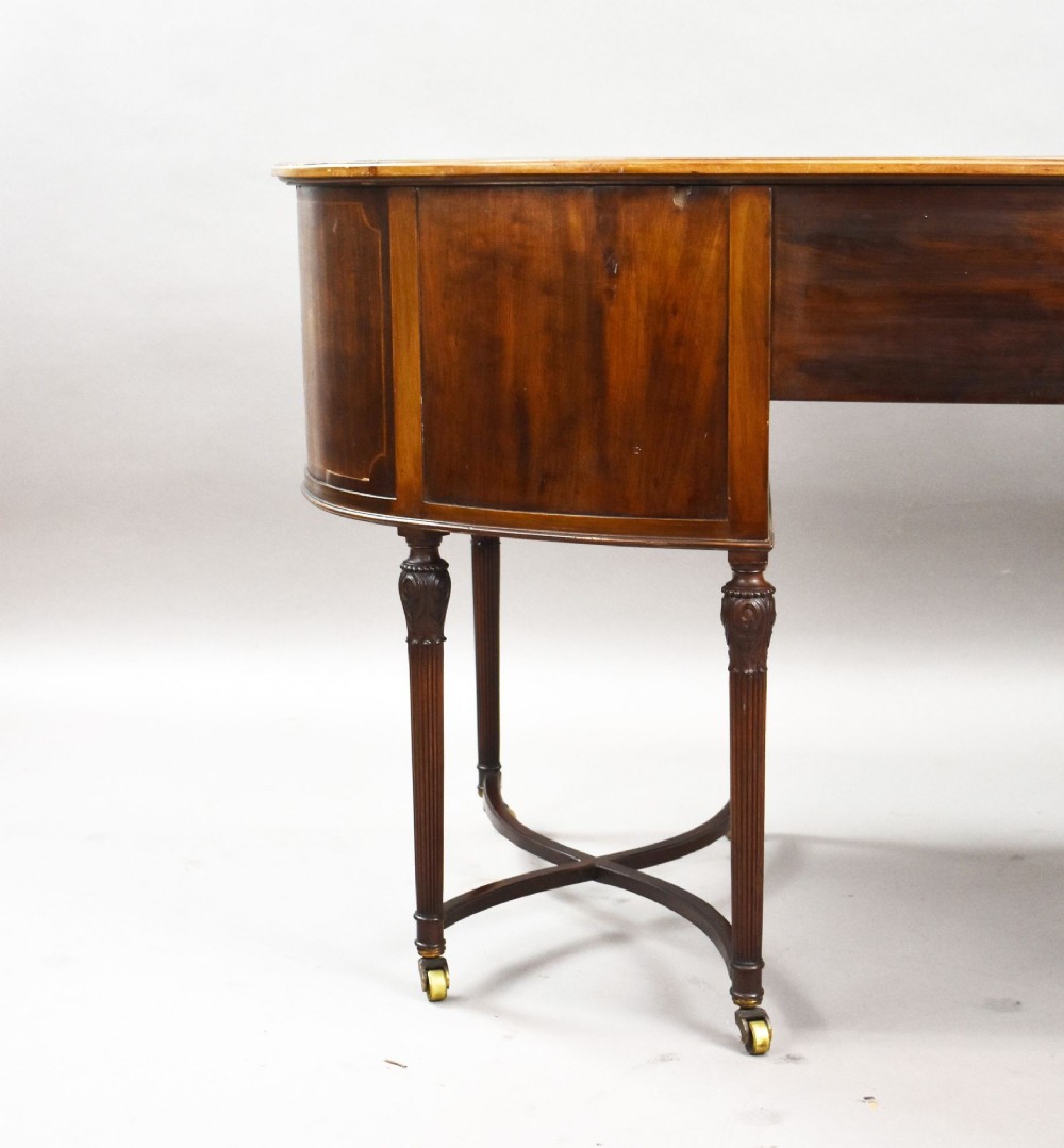 An Edwardian kidney-shaped writing desk crafted from flame mahogany with a green leather writing surface, five drawers, turned fluted legs, and brass castors. View X