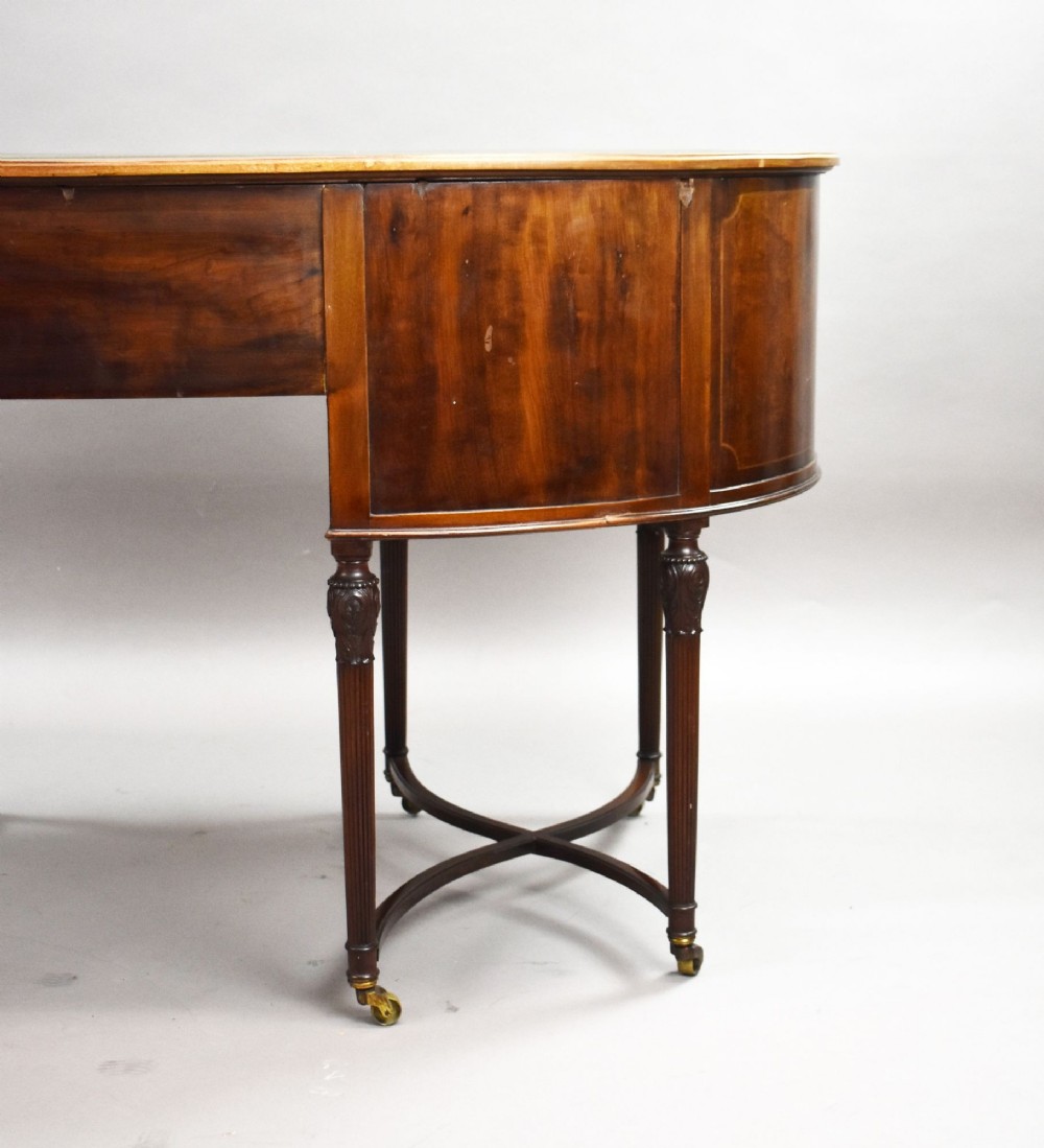An Edwardian kidney-shaped writing desk crafted from flame mahogany with a green leather writing surface, five drawers, turned fluted legs, and brass castors. View XI