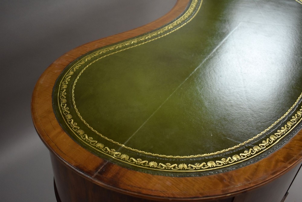 An Edwardian kidney-shaped writing desk crafted from flame mahogany with a green leather writing surface, five drawers, turned fluted legs, and brass castors. View XII