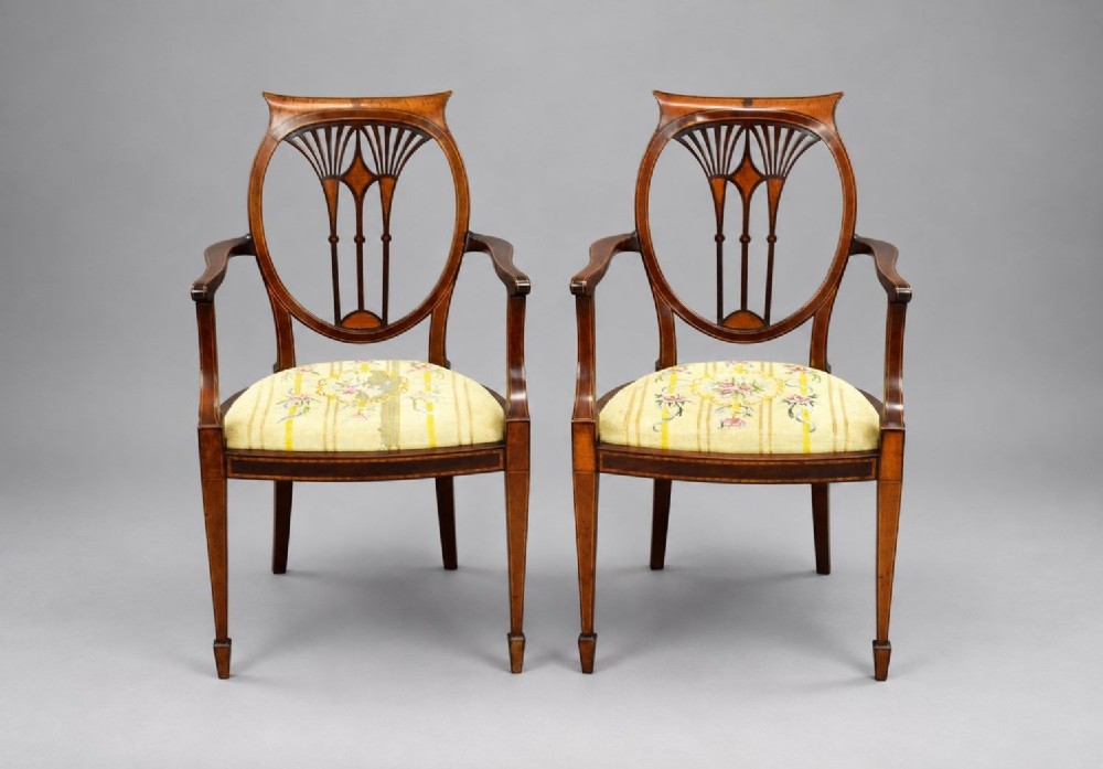 A pair of Edwardian Sheraton Revival mahogany armchairs featuring oval backs with vertical fan splats, swept arms, satinwood inlays, and yellow floral upholstered seats.