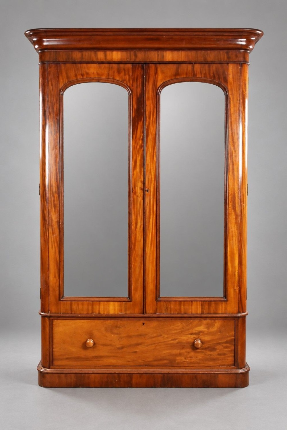 A nineteenth-century Victorian mahogany wardrobe featuring two arched mirrored doors above a single full-width drawer with turned wooden knobs.