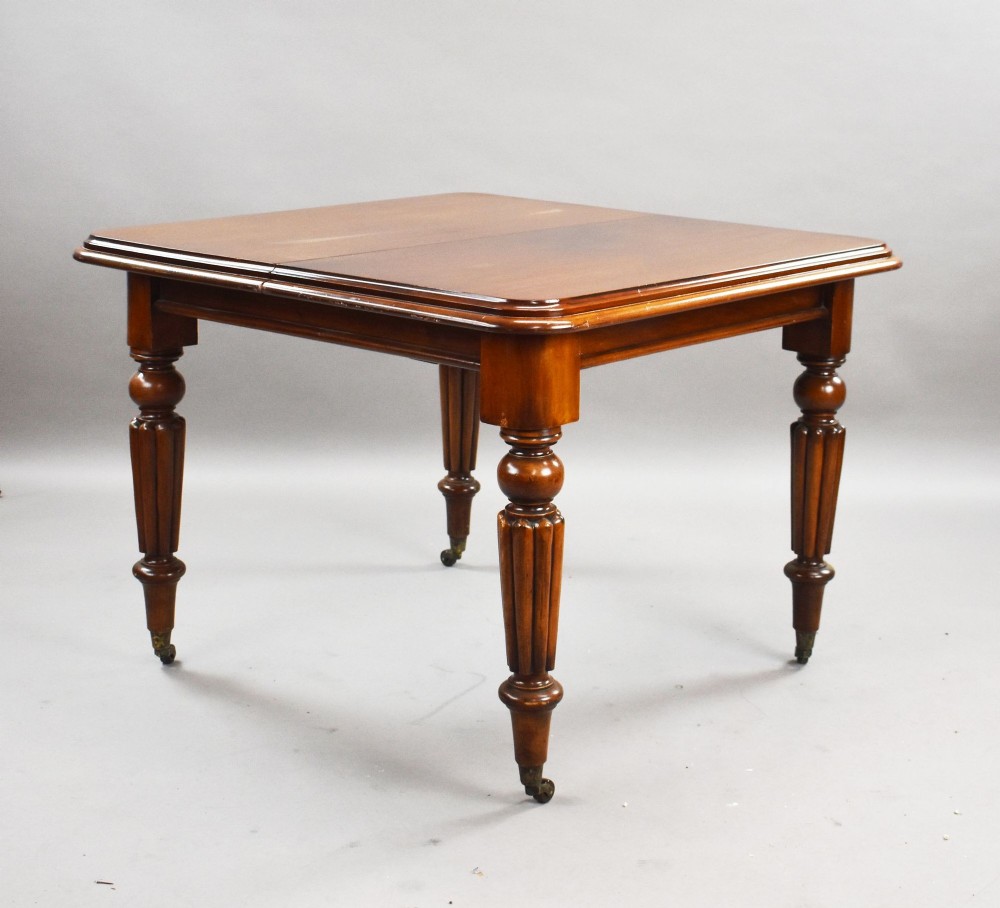 A Victorian mahogany extending dining table featuring fluted turned legs set on brass castors. View III