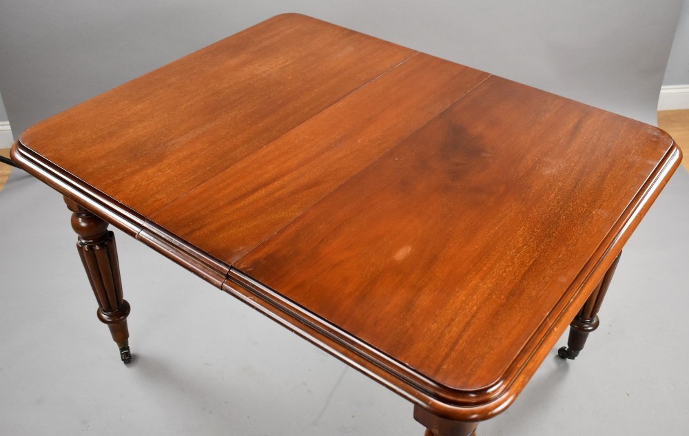 A Victorian mahogany extending dining table featuring fluted turned legs set on brass castors. View IV