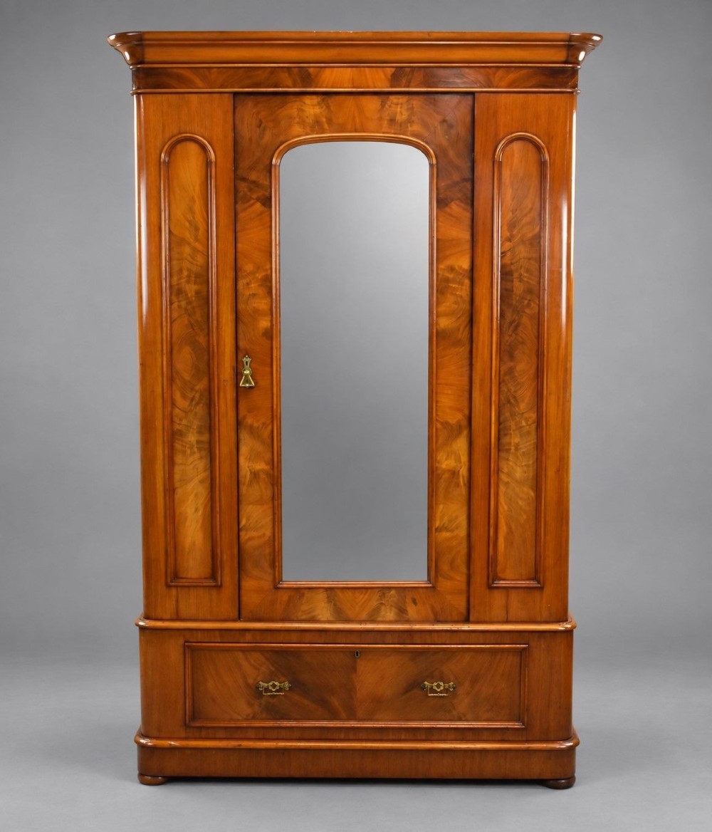 Victorian flame mahogany wardrobe featuring a central full-length arched mirror door flanked by arched wood panels, topped with a moulded cornice and resting on a base drawer.