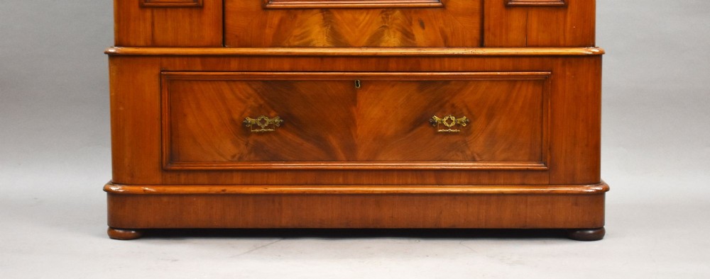Victorian flame mahogany wardrobe featuring a central full-length arched mirror door flanked by arched wood panels, topped with a moulded cornice and resting on a base drawer. View V