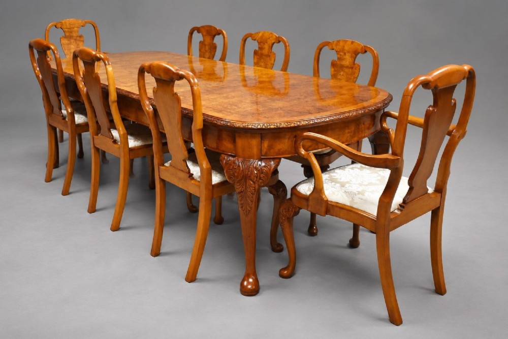 A Queen Anne style burr walnut extending dining table shown with eight matching chairs featuring curved backrests and floral upholstered seats.