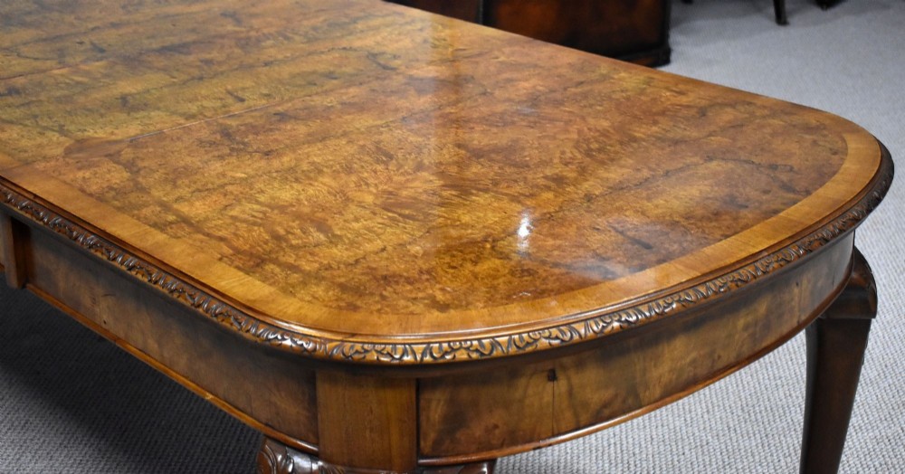 A Queen Anne style burr walnut extending dining table shown with eight matching chairs featuring curved backrests and floral upholstered seats. View VII