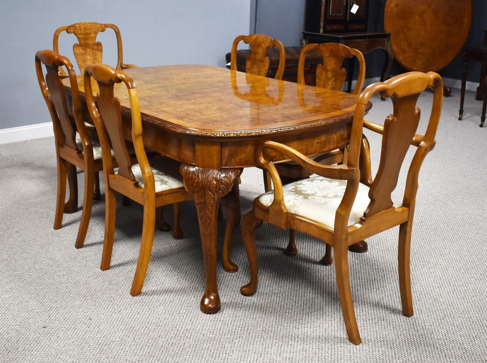 A Queen Anne style burr walnut extending dining table shown with eight matching chairs featuring curved backrests and floral upholstered seats. View VIII