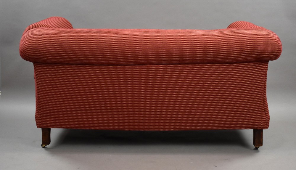 A late Victorian upholstered two-seater sofa featuring red striped fabric, scroll arms, and turned wooden legs with brass castors. View V