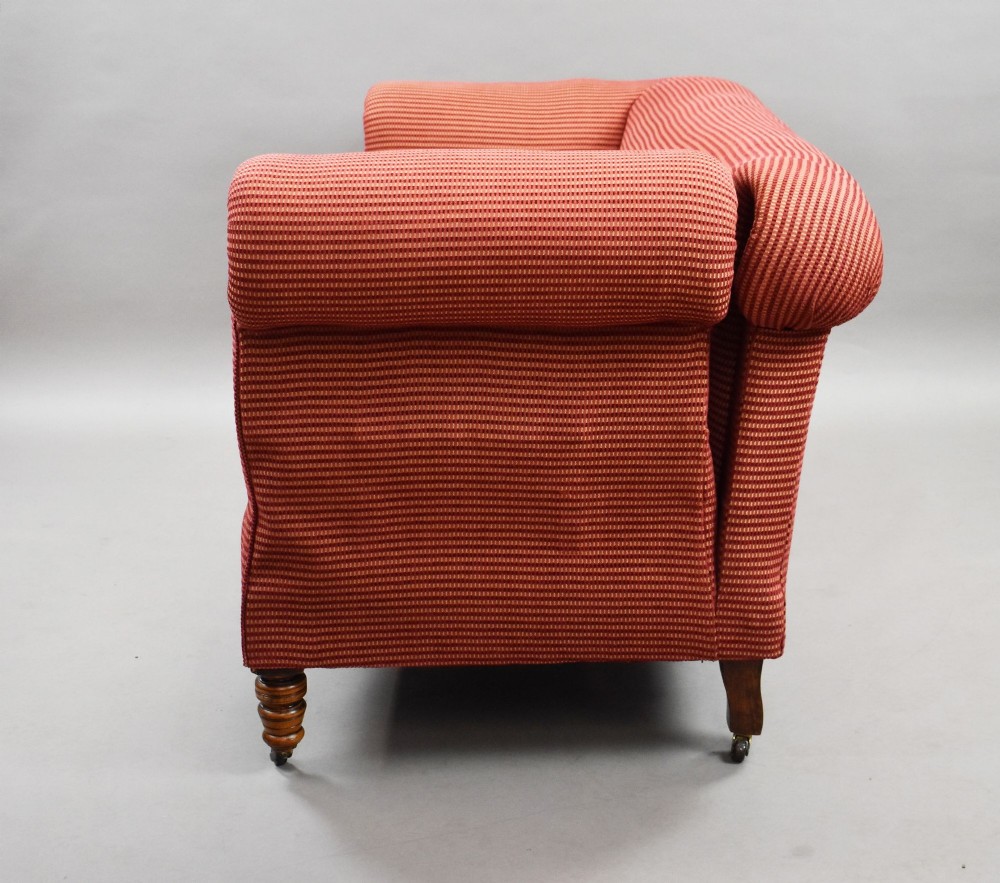 A late Victorian upholstered two-seater sofa featuring red striped fabric, scroll arms, and turned wooden legs with brass castors. View VI