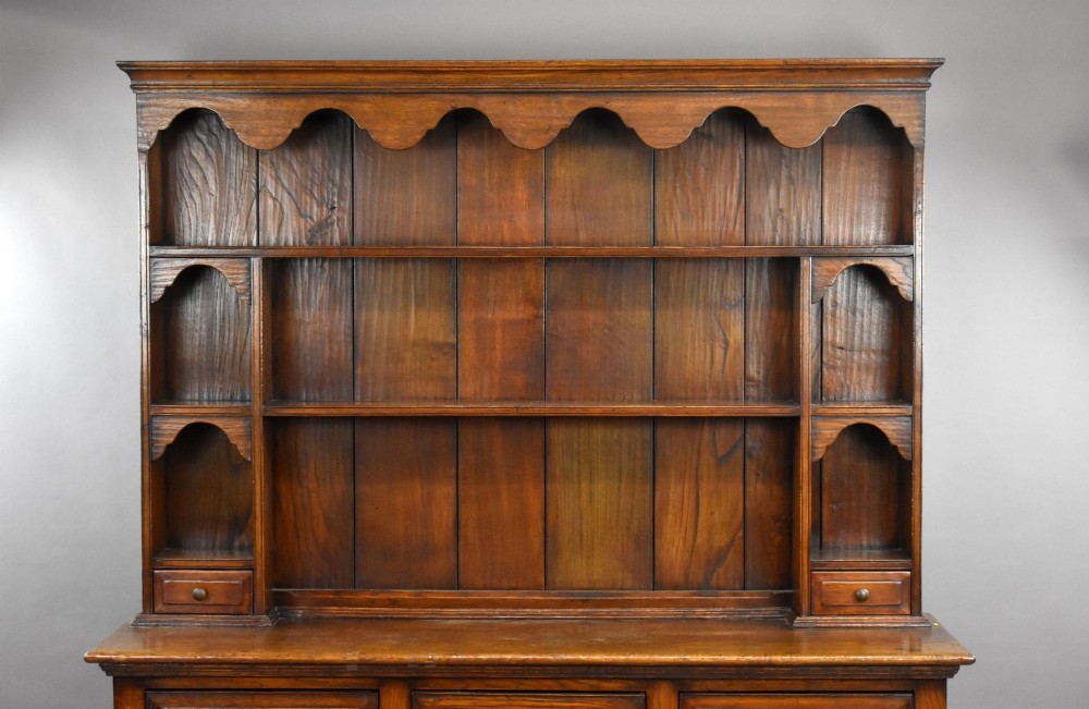A warm brown oak Welsh dresser featuring an open tiered rack with scalloped aprons above three drawers and a potboard base on turned legs. View II