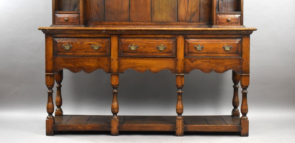 A warm brown oak Welsh dresser featuring an open tiered rack with scalloped aprons above three drawers and a potboard base on turned legs. View III