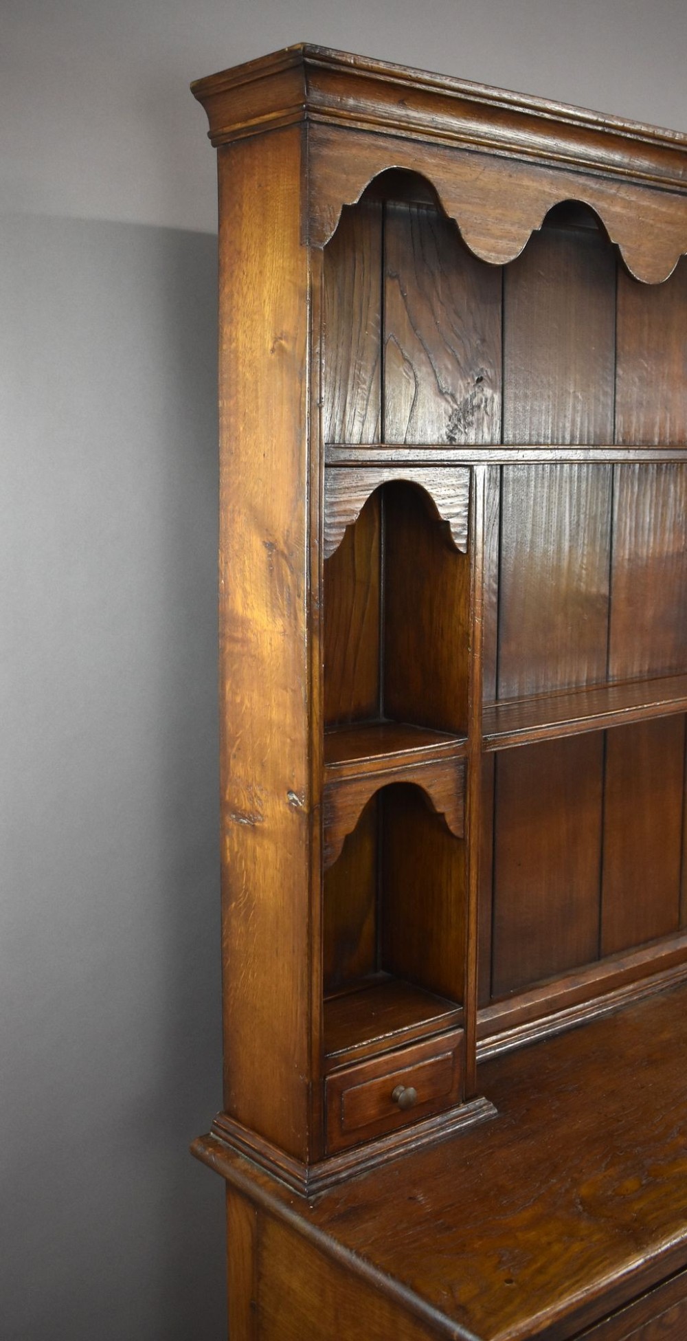 A warm brown oak Welsh dresser featuring an open tiered rack with scalloped aprons above three drawers and a potboard base on turned legs. View IV