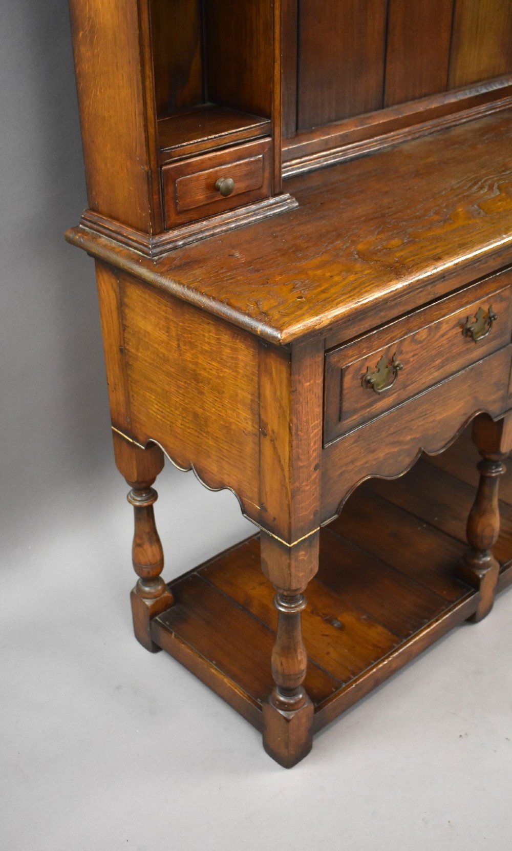 A warm brown oak Welsh dresser featuring an open tiered rack with scalloped aprons above three drawers and a potboard base on turned legs. View V
