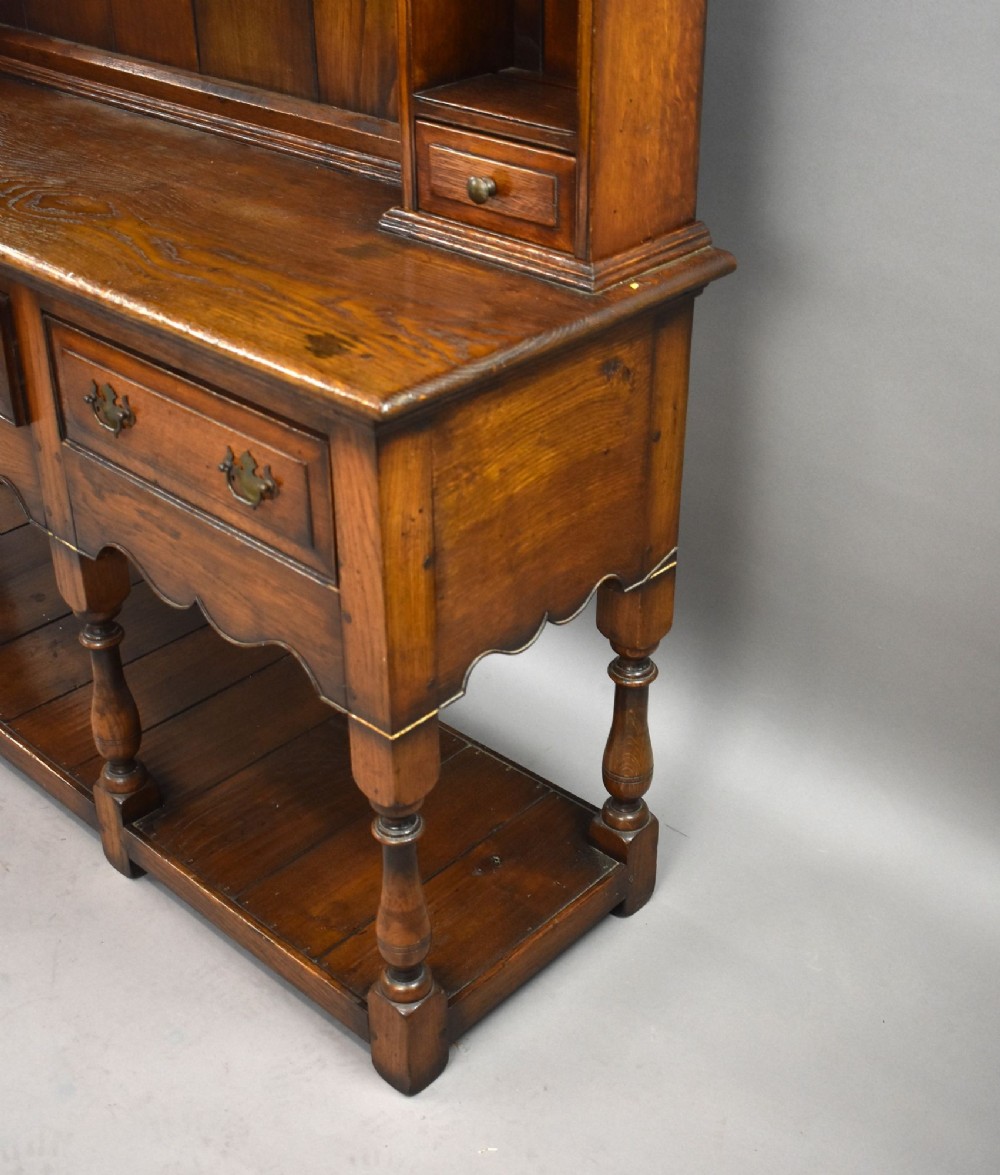 A warm brown oak Welsh dresser featuring an open tiered rack with scalloped aprons above three drawers and a potboard base on turned legs. View VII