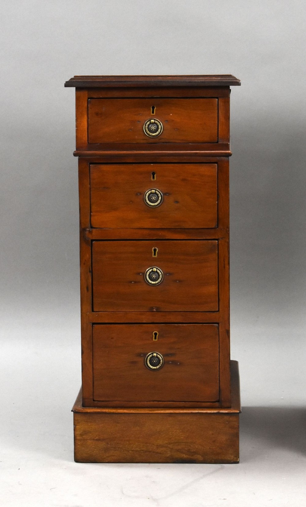 A matching pair of narrow Victorian mahogany bedside chests, each featuring four stacked drawers with central brass ring pulls set on a solid plinth base. View V
