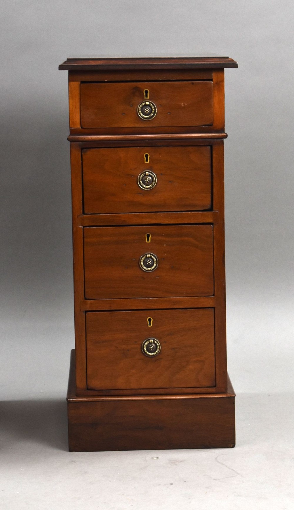 A matching pair of narrow Victorian mahogany bedside chests, each featuring four stacked drawers with central brass ring pulls set on a solid plinth base. View VI