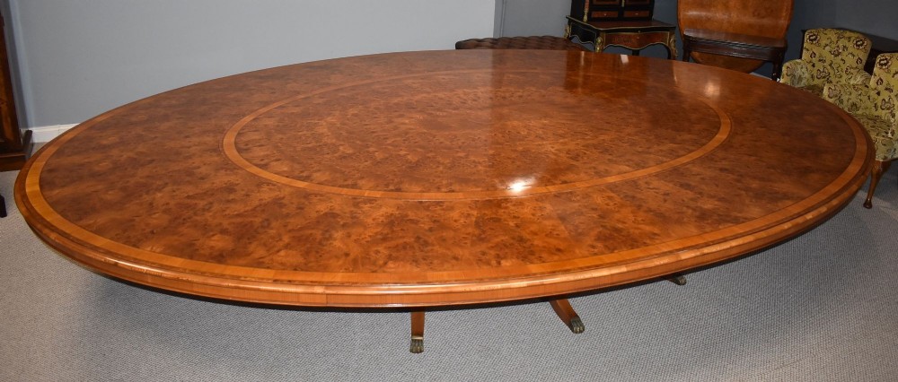 A large oval burr walnut extending dining table with inlaid crossbanding and pedestal legs terminating in brass castors. View VI
