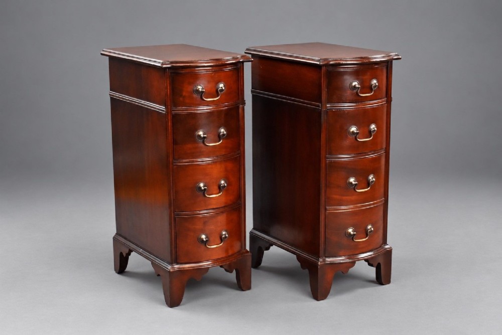 A pair of narrow mahogany bow-front bedside chests featuring four drawers each with brass drop handles and bracket feet.