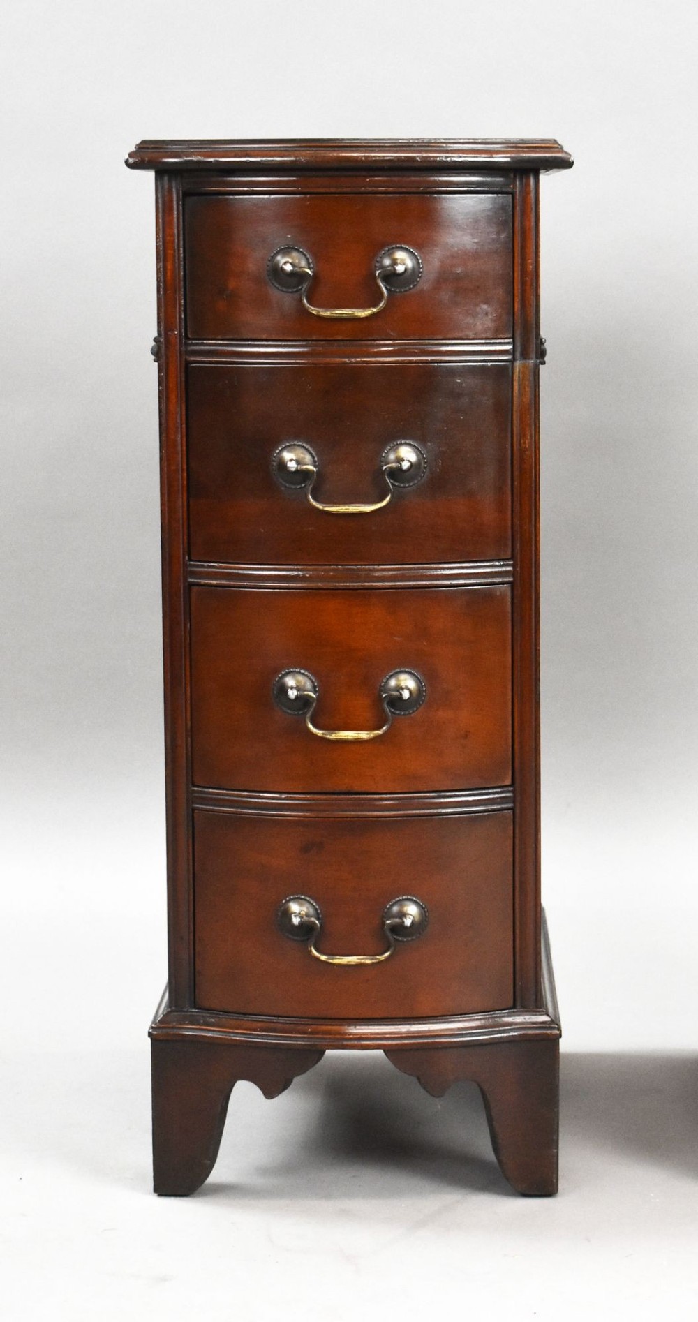 A pair of narrow mahogany bow-front bedside chests featuring four drawers each with brass drop handles and bracket feet. View V