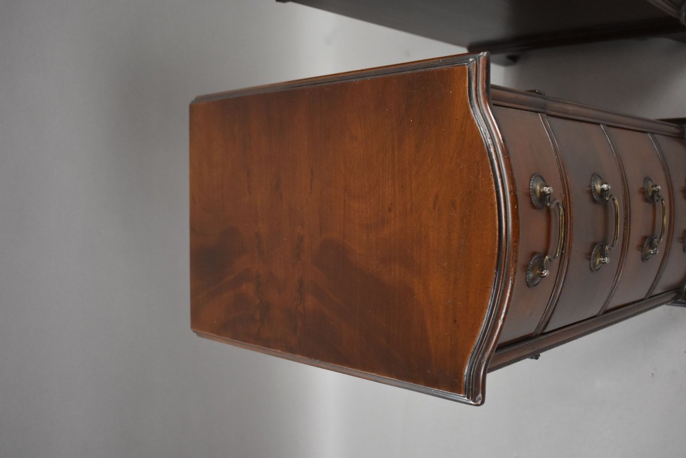 A pair of narrow mahogany bow-front bedside chests featuring four drawers each with brass drop handles and bracket feet. View VII