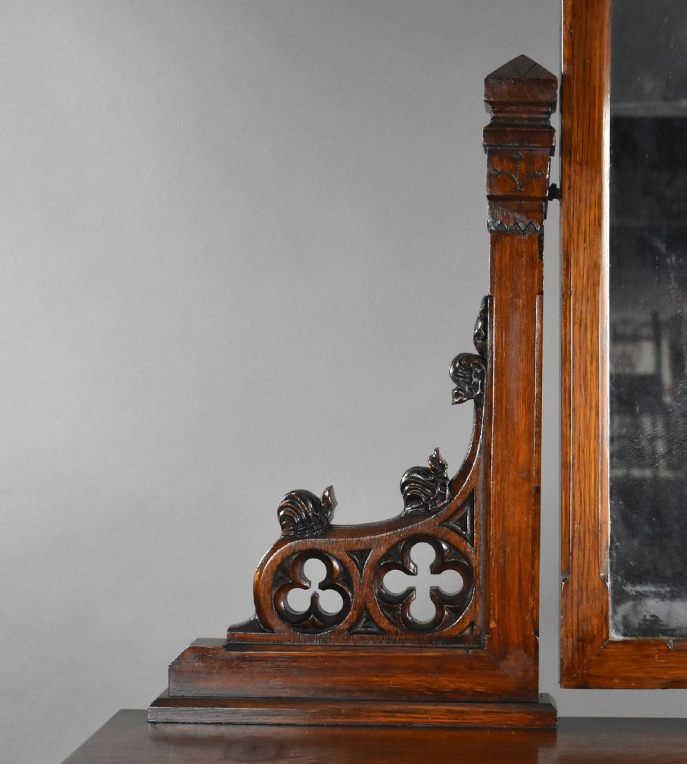 A Victorian Gothic Revival oak dressing table featuring a central pointed arched mirror, trefoil tracery carvings, multiple drawers, and pedestal cupboards with diagonal wood panelling. View X