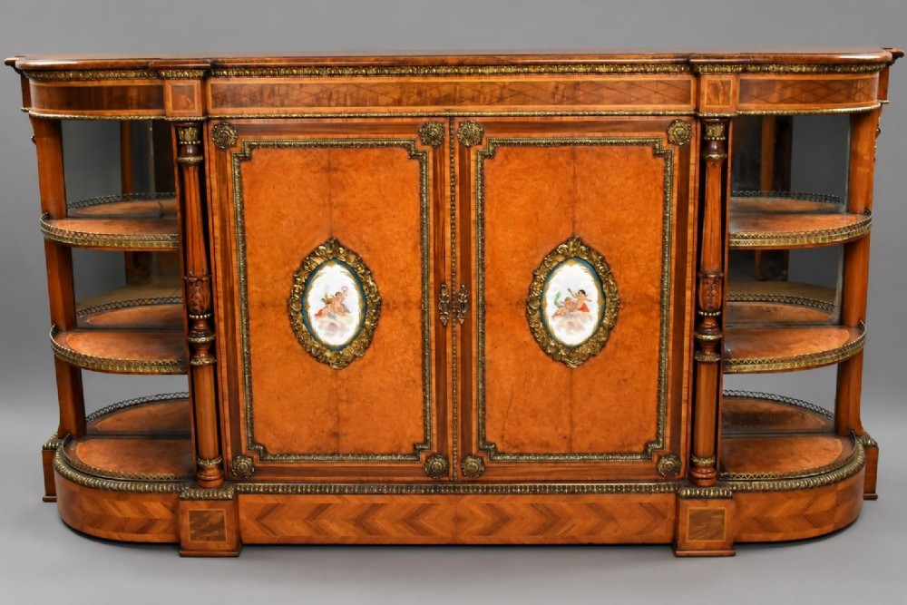 A Victorian burr walnut credenza featuring central cupboard doors with oval porcelain plaques and gilt bronze mounts flanked by curved open display shelves.