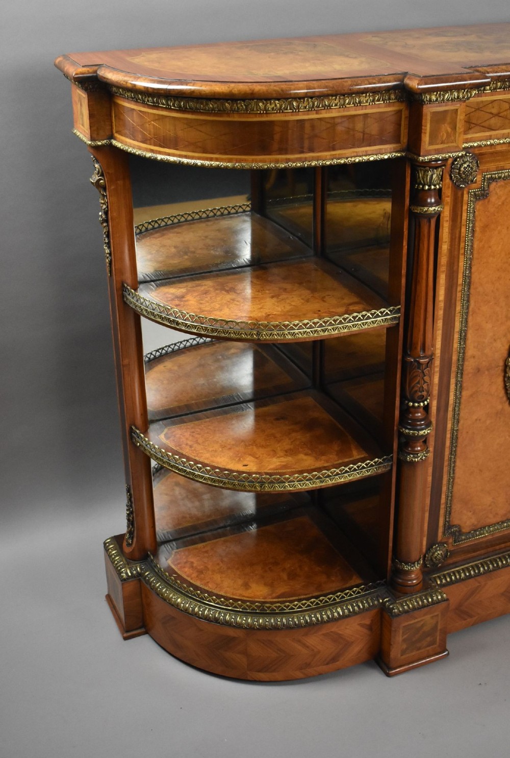 A Victorian burr walnut credenza featuring central cupboard doors with oval porcelain plaques and gilt bronze mounts flanked by curved open display shelves. View II
