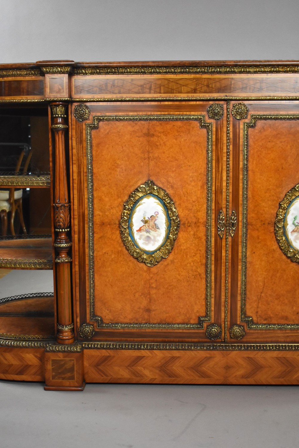 A Victorian burr walnut credenza featuring central cupboard doors with oval porcelain plaques and gilt bronze mounts flanked by curved open display shelves. View III