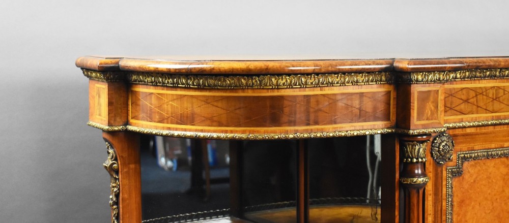 A Victorian burr walnut credenza featuring central cupboard doors with oval porcelain plaques and gilt bronze mounts flanked by curved open display shelves. View VI