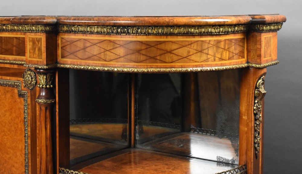 A Victorian burr walnut credenza featuring central cupboard doors with oval porcelain plaques and gilt bronze mounts flanked by curved open display shelves. View IX