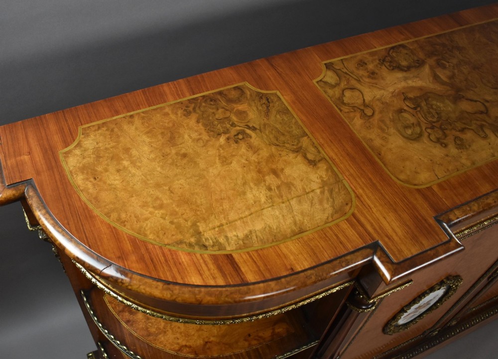 A Victorian burr walnut credenza featuring central cupboard doors with oval porcelain plaques and gilt bronze mounts flanked by curved open display shelves. View XII