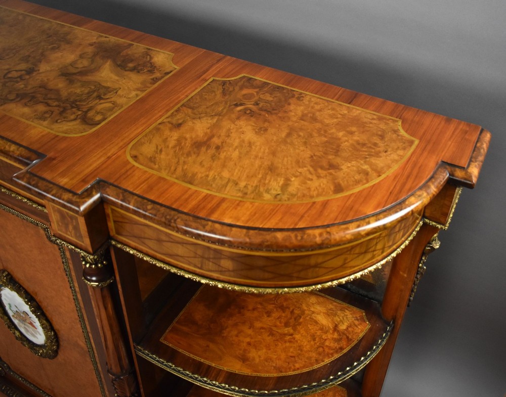 A Victorian burr walnut credenza featuring central cupboard doors with oval porcelain plaques and gilt bronze mounts flanked by curved open display shelves. View XIV