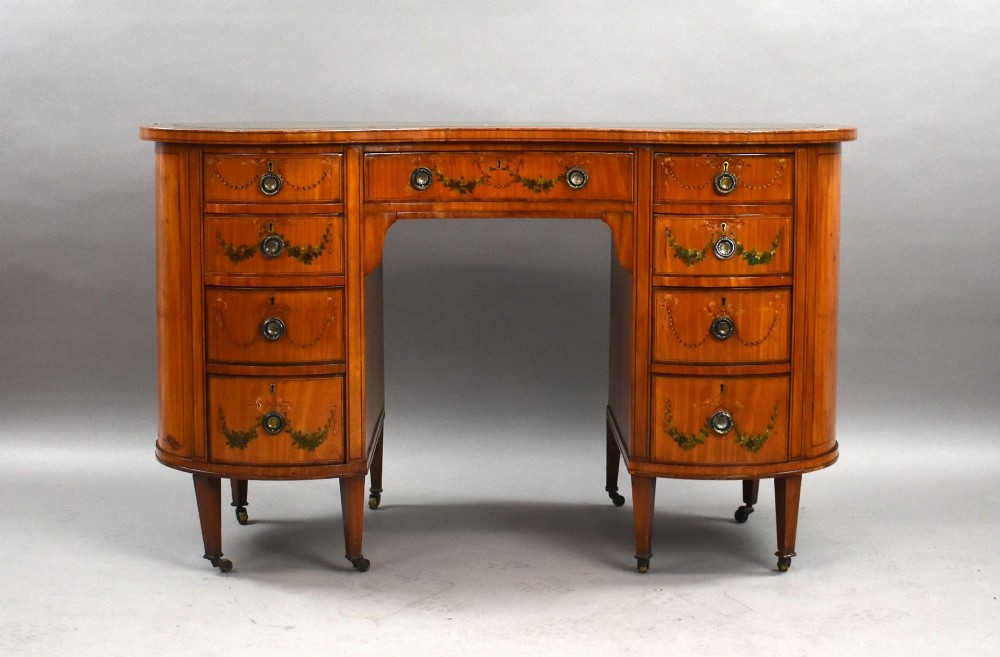 An Edwardian satinwood kidney-shaped writing desk featuring nine hand-painted drawers with brass ring handles and tapered legs on castors. View II